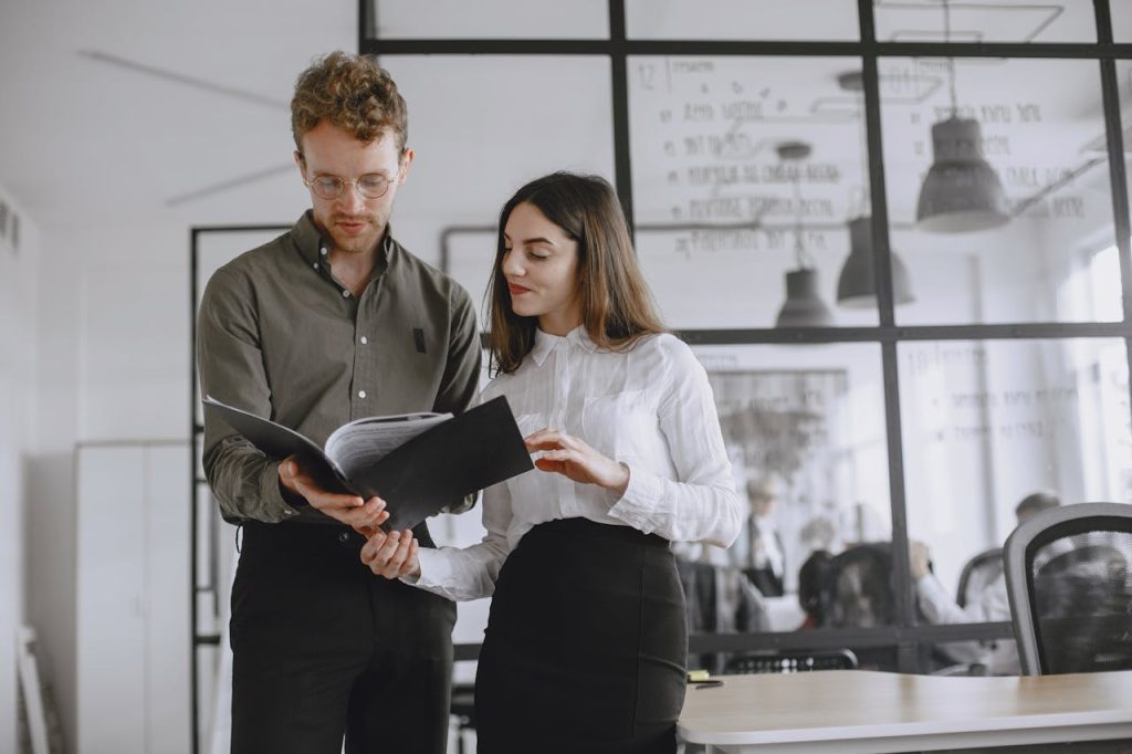 Two professionals discuss documents in a modern office environment.